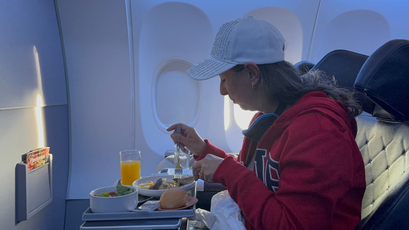 Kharol almoçando na classe executiva da Copa, com a janela do avião ao fundo, entre Orlando e a Cidade do Panamá